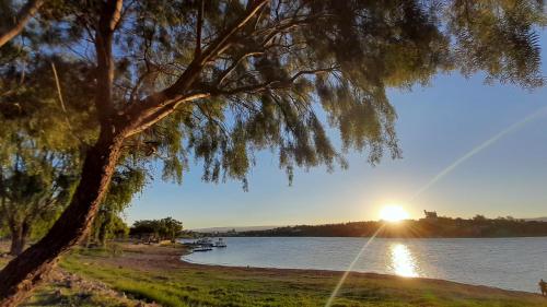 a tree in front of a lake with the sunset at Duplex Villa Carlos Paz in Villa Carlos Paz