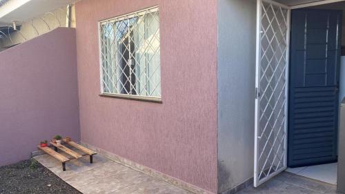 a house with a pink wall with a window and a bench at Casa com garagem 4 pessoas in Ponta Grossa