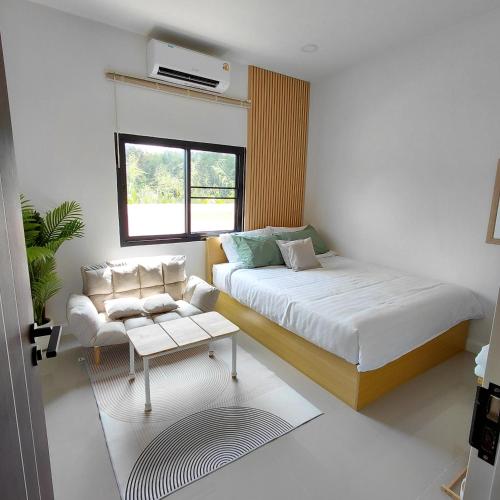 a bedroom with a bed and a couch and a table at Baanjaifu บ้านใจฟู in Ban Muang Ba