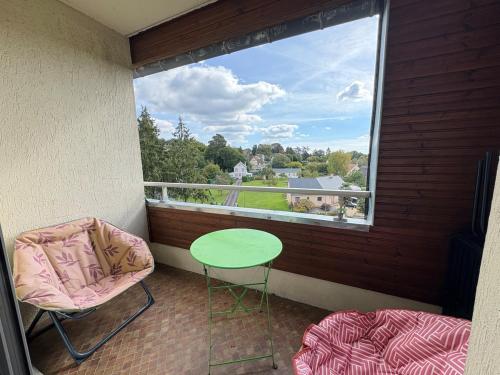 balcón con mesa verde, sillas y ventana en Studio cosy avec balcon, en Bagnoles de l'Orne