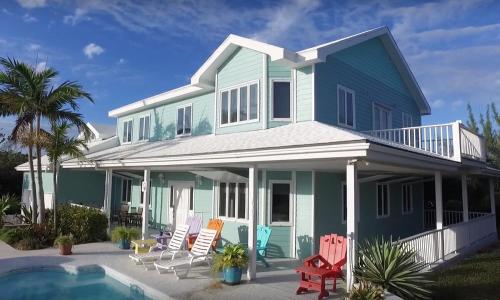 a blue house with chairs and a swimming pool at Bahamian Rhapsody of Hopetown, Elbow Cay, Abaco,BA 