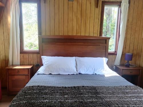 1 dormitorio con 1 cama con cabecero de madera y 2 ventanas en Cabañas CyG - Chaitén, en Chaitén