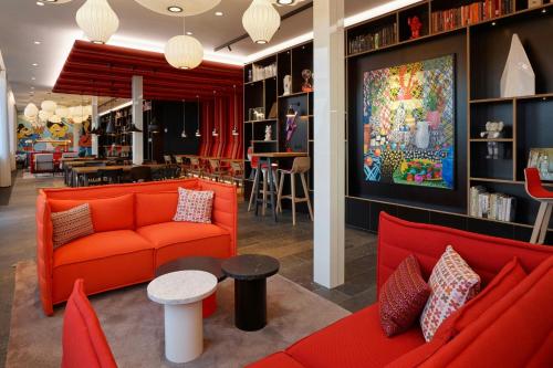 a living room with red couches and a restaurant at citizenM Copenhagen Radhuspladsen in Copenhagen