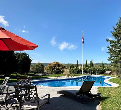 a swimming pool with chairs and a red umbrella at Mountain Ash Country Manor and Spa in Creemore