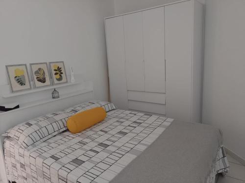 a white bedroom with a bed with a yellow pillow at Lugar encantado - Apartamento in Brasilia