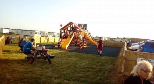 スケッグネスにあるE12 jeans caravan The Chaseの遊び場の横にあるピクニックテーブルに座っている人々のグループ