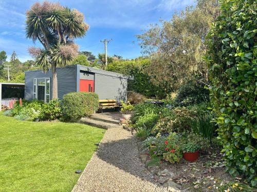 a tiny house with a red door in a garden at Brighton Beach in Dunedin