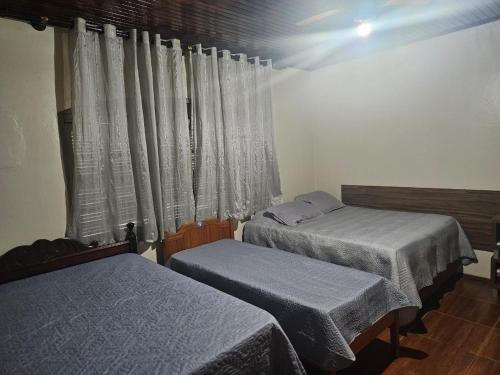Cette chambre comprend deux lits et une fenêtre avec des rideaux. dans l'établissement morada da felicidade, à São Gabriel