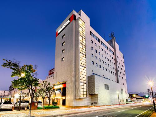 a tall white building with a red arrow on it at APA Hotel Yamagata Tsuruoka Ekimae in Tsuruoka