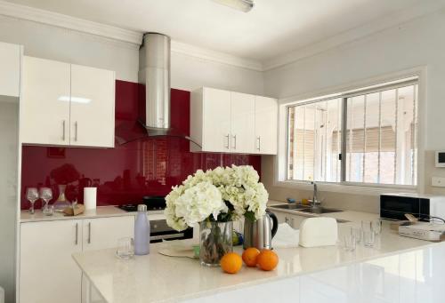 Burwood Family Guest Home في سيدني: مطبخ مع خزائن بيضاء و إناء من الزهور على منضدة