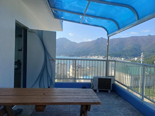 a balcony with a wooden table and a view of the mountains at Melodia Pension in Geoje 