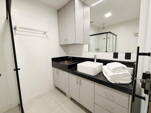 a white bathroom with a sink and a mirror at Studio Soberano - O mais luxuoso de CG in Campo Grande
