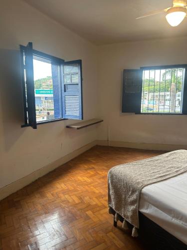 a bedroom with a bed and two windows and a wooden floor at Oxx Quarto Terra in Congonhas