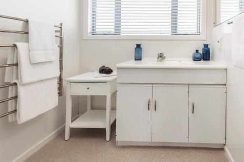 a white bathroom with a sink and a mirror at Holiday on Hamblyn - 2 BR home near Fitzroy Beach in New Plymouth