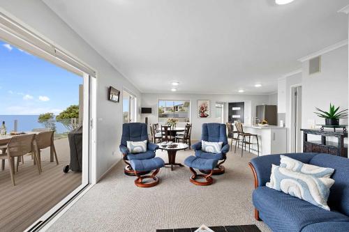 a living room with blue chairs and a dining room at Beachfront Breeze - sea views for days in New Plymouth