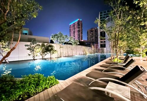 a pool with lounge chairs in a city at night at Lucentia Suites klcc by SkyPool in Kuala Lumpur