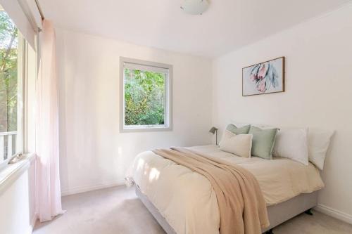 ein weißes Schlafzimmer mit einem Bett und einem Fenster in der Unterkunft Cosy 2 Bedroom Cottage with spabath and fireplace in Mount Dandenong