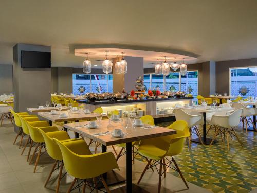 a restaurant with tables and yellow chairs and a kitchen at KHAS Malioboro Hotel in Yogyakarta
