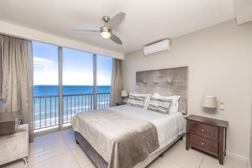 a bedroom with a bed and a balcony with the ocean at Infinity Self Catering Apartments in Bloubergstrand