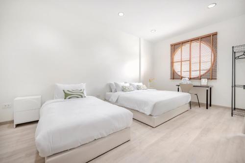 a white bedroom with two beds and a window at Haus Ekkamai 2 in Klong Toi