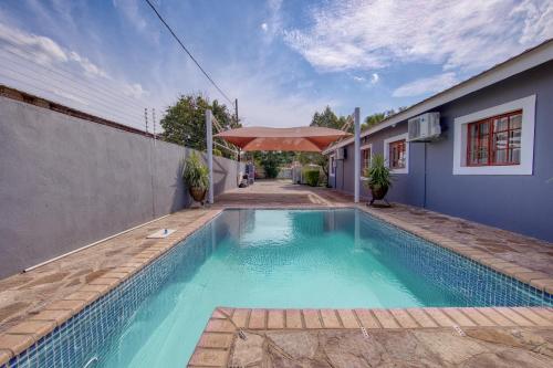a swimming pool with an umbrella next to a house at White Rose Villa in Gaborone