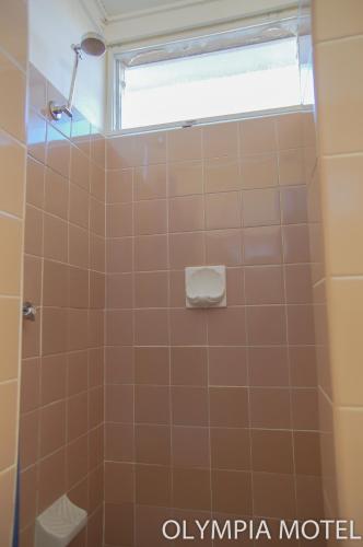 a bathroom with a tiled shower with a window at Olympia Motel in Queanbeyan