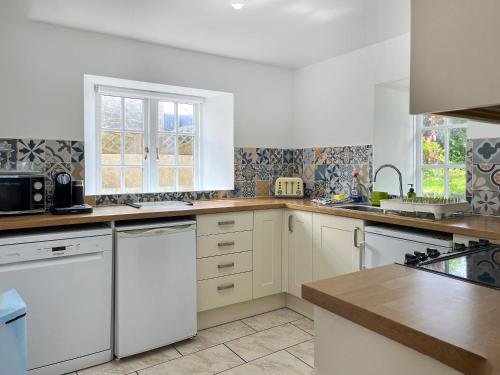 une cuisine avec des armoires blanches et des appareils électroménagers blancs dans l'établissement Bluebell Cottage, à South Brent