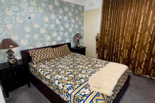 2 Bedroom Apartment - Sleeps 4 Free Parking Wifi في Pollokshaws: غرفة نوم مع سرير بجدار نمط الزهور