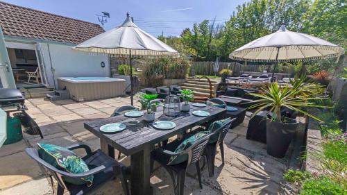 une terrasse avec une table en bois, des chaises et des parasols dans l'établissement Shippenrill Croyde - Sleeps 14 - Hot Tub option - Stylish Home with fire pit, table tennis & dog friendly, à Croyde