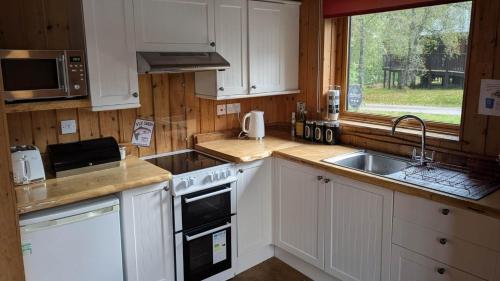 a kitchen with white cabinets and a sink and a window at Bracken Lodge in Dalavich