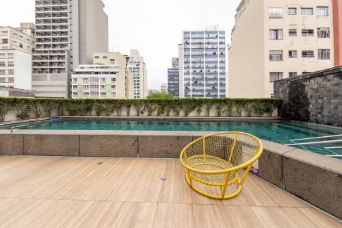 une chaise jaune posée sur le toit d'un immeuble avec piscine dans l'établissement B Homy Genebra, à São Paulo