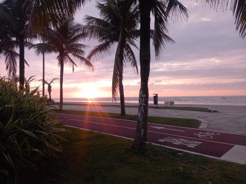 a sunset at the beach with palm trees at Frente ao mar, conforto e paz apto 12 in Praia Grande