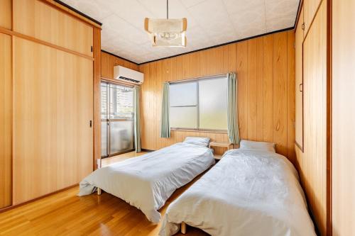 two beds in a room with wooden walls and a window at まほら in Fukuoka
