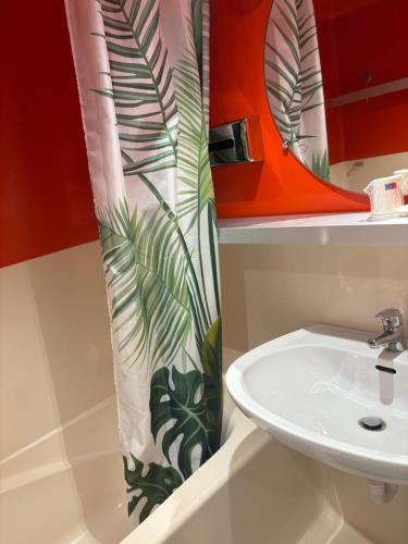 a bathroom with a sink and a shower curtain at Hotel Couleurs Sud Centre-ville Gare Charleville-Mézières in Charleville-Mézières