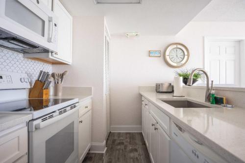 a kitchen with white cabinets and a sink and a clock at Tortuga Suite at Sunrise Suites Resort - Heated Pool, Hot Tub & Free Parking in Key West