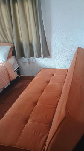 a bed with an orange comforter in a bedroom at Quarto com Ar à 500m da praia Espaco Aconchego do Gugu in Arraial do Cabo