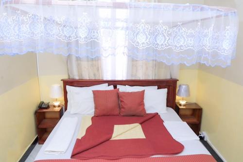 1 cama con almohadas rojas y blancas y ventana en M3 Stella Hotel, en Kampala