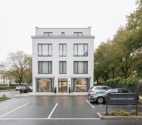 een wit gebouw met auto's geparkeerd op een parkeerplaats bij Takes Antalya Apart in Antalya