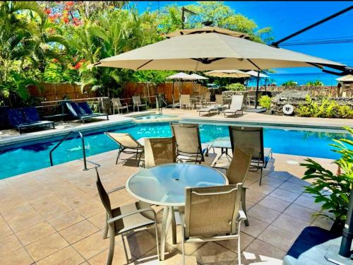 a table with chairs and an umbrella next to a pool at 2b2b AC Magic Tides Kona near Magic Sands Beach in Kailua-Kona