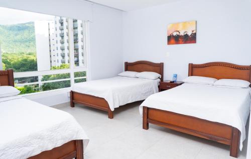 two beds in a white room with a window at Sanha Plus Hotel in Santa Marta