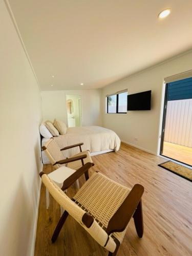 a bedroom with two beds and chairs and a television at The Coconut Hut Papamoa Beach in Tauranga