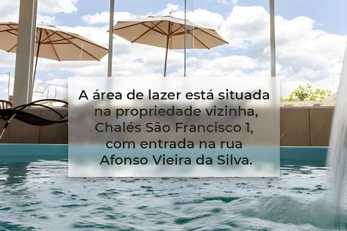 a sign next to a swimming pool with umbrellas at Chalés São Francisco I in Santo Antônio do Pinhal