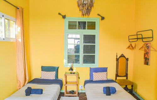 Dos camas en una habitación amarilla con ventana. en La Maison ZiaZen, en Porto da Cruz