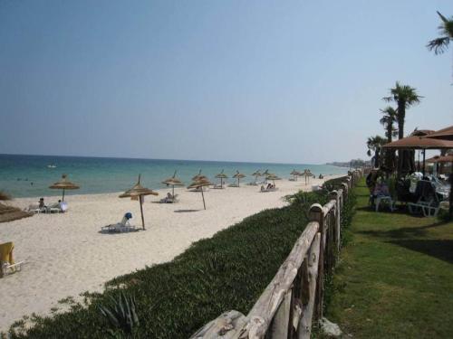 a beach with umbrellas and people sitting on the sand at Résidence Sayadi - Chatt Meriam - Sousse in Port El Kantaoui