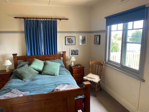 a bedroom with a bed with blue sheets and a window at The Cottage at Raheen in Mallacoota