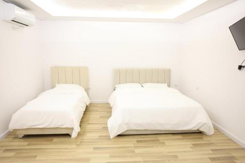 two beds in a room with white walls and wooden floors at The Central Spot in Tirana