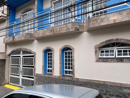 ein Gebäude mit blauen Fenstern und einem Auto, das vorne parkt in der Unterkunft Casa Nhá Chica - Aparecida - a 10 minutos a pé do Santuário Nacional in Aparecida