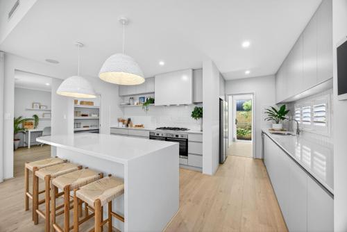 a white kitchen with a white counter and stools at Coastal Luxe 4-Bed House in Madora Bay in Singleton