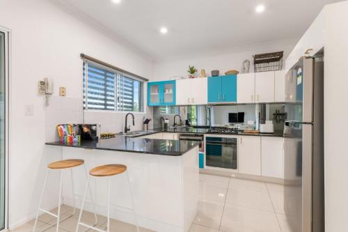 a white kitchen with blue cabinets and stools at Spacious 2-Bed with Private Rooftop & BBQ Access in Brisbane
