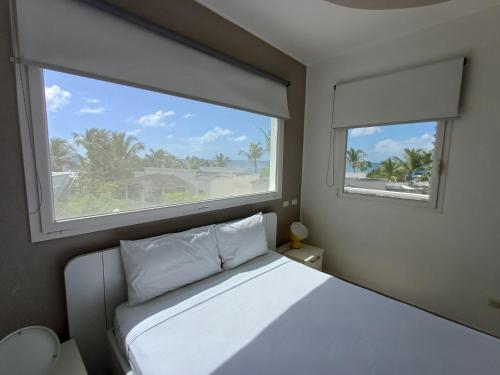 a bedroom with a white bed and two windows at TRACADERO Beach Club & Holidays Rentals in Bayahibe
